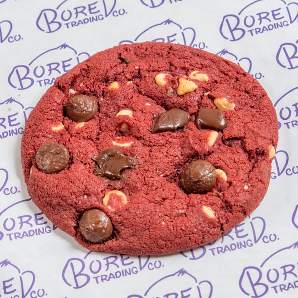 A red velvet cookie with chocolate and white chocolate chips on Bored Trading Co. branded paper.