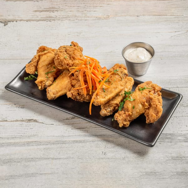 Crispy fried chicken wings with shredded carrots and a side of ranch dressing on a black plate.