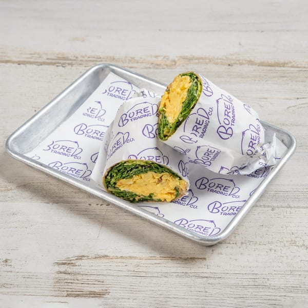 Two Bored Trading Cafe breakfast wraps with scrambled eggs and greens on a metal tray.